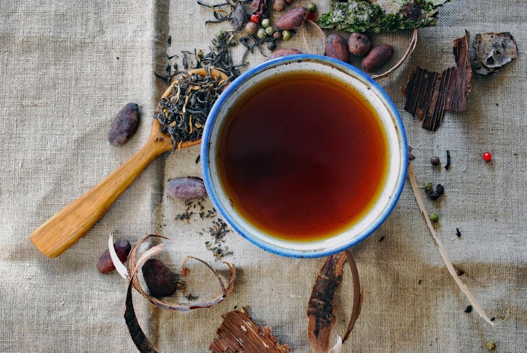 Cup of herbal tea with loose leaves, spices, and cocoa beans on rustic fabric